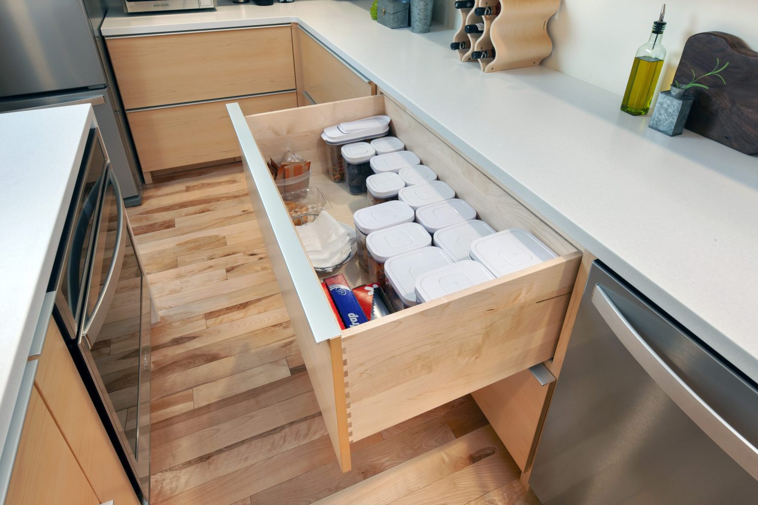 Open deep kitchen drawer holding food storage containers beside a dishwasher