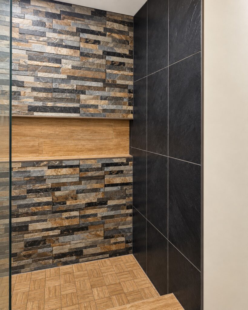 Stacked stone accent wall with a floating wood shelf in a rustic modern walk-in shower