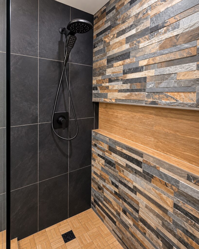 Walk-in shower with dark tile, matte black rainfall showerhead, and stacked stone accent wall