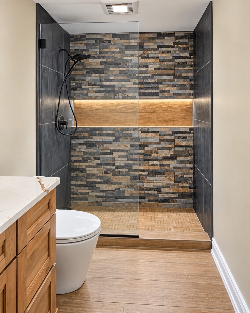 Rustic modern bathroom remodel with a stacked stone accent wall, backlit wood niche, and freestanding soaking tub
