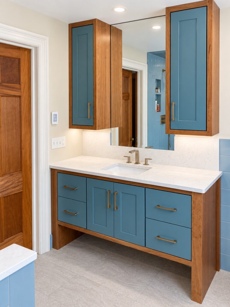 Blue bathroom cabinets with cherry wood frames and a mirrored wall reflecting the marble shower across the room