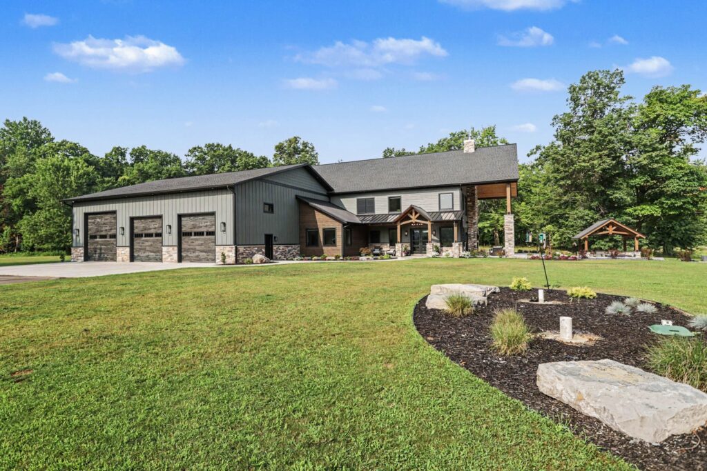 Daytime exterior of a custom KCH Homes build with a three-car garage, gabled metal roof, board-and-batten and stone siding, and fresh landscaping