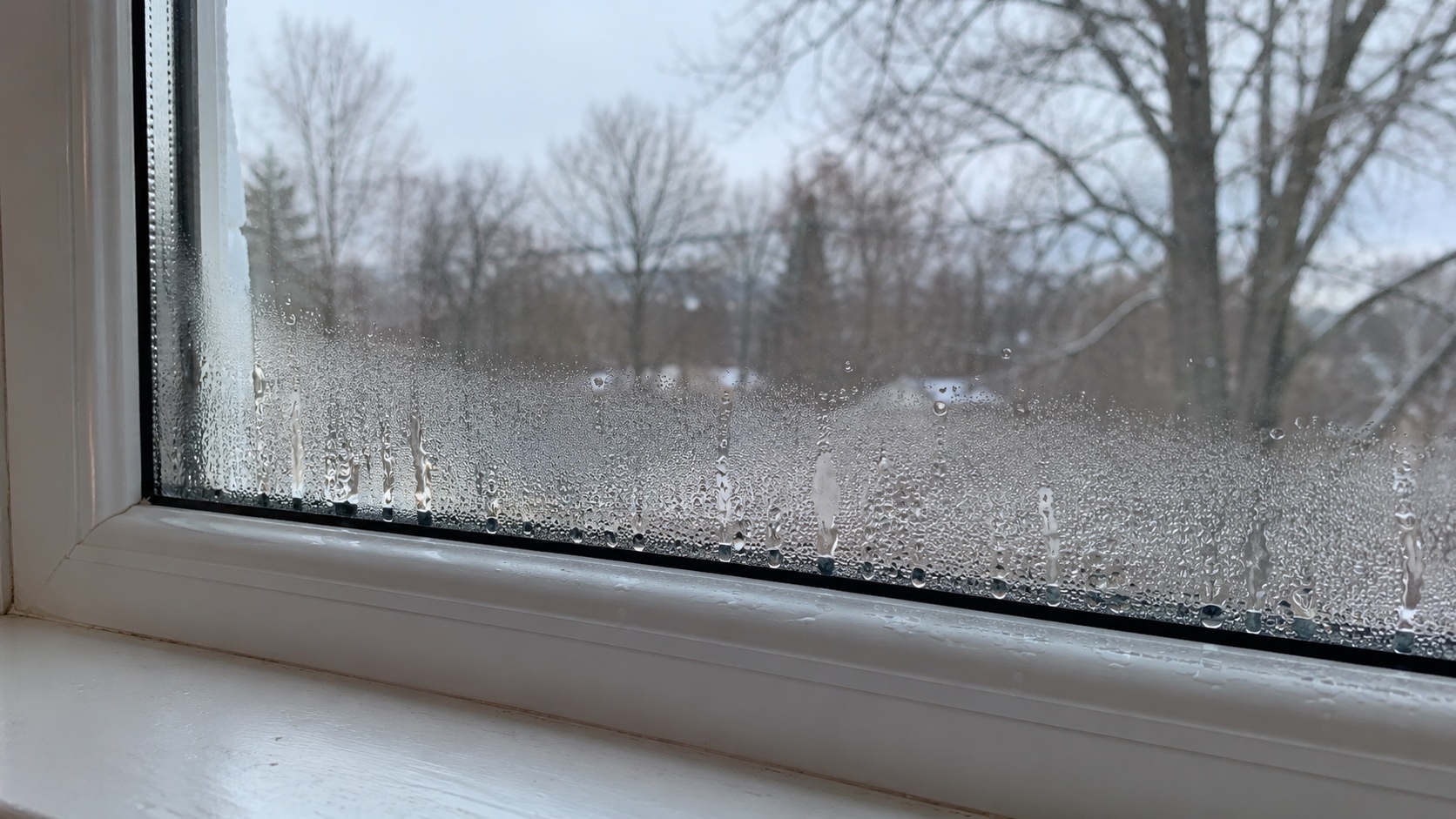Interior window condensation with water droplets collecting along the lower glass and white sill