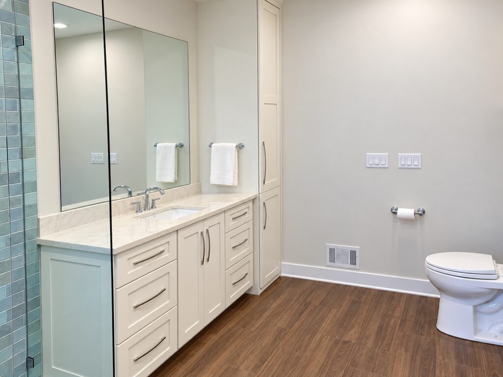White bathroom vanity and tall storage cabinet with a light countertop, large mirror and blue-green shower tile.