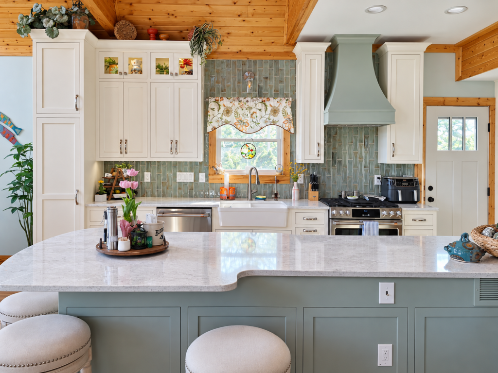 Front view of a sage island facing cream cabinetry, a farmhouse sink and matching sage range hood.