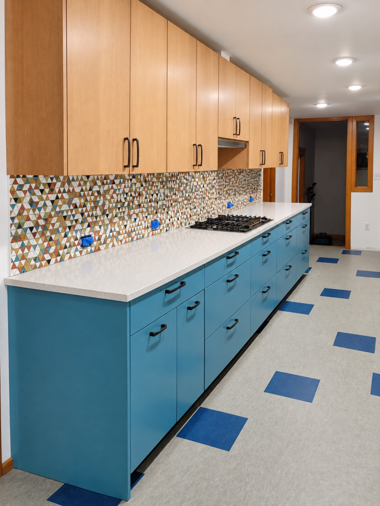 Blue base cabinets and wood upper cabinets with a gas cooktop and multicolored triangular tile backsplash.