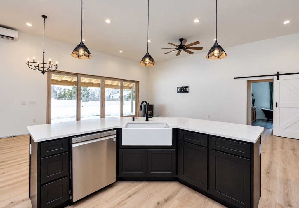 White farmhouse sink and stainless dishwasher in a dark angled kitchen island, with patio doors and a white barn door behind.