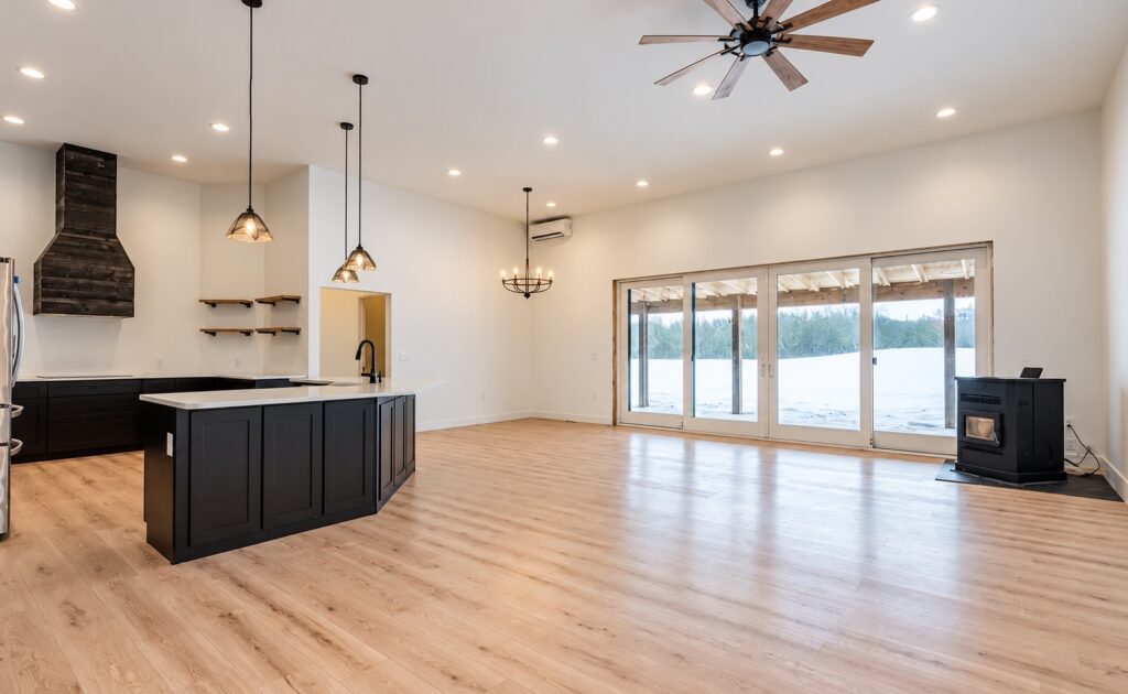 Open living area with light wood flooring, a dark kitchen island, wide glass patio doors and a black stove.