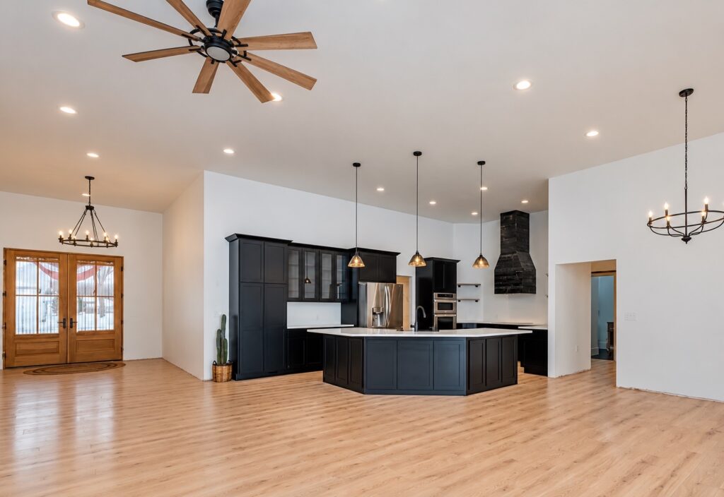 Wide view of an open-plan kitchen with dark cabinetry, an angled island, white countertops and wood flooring.